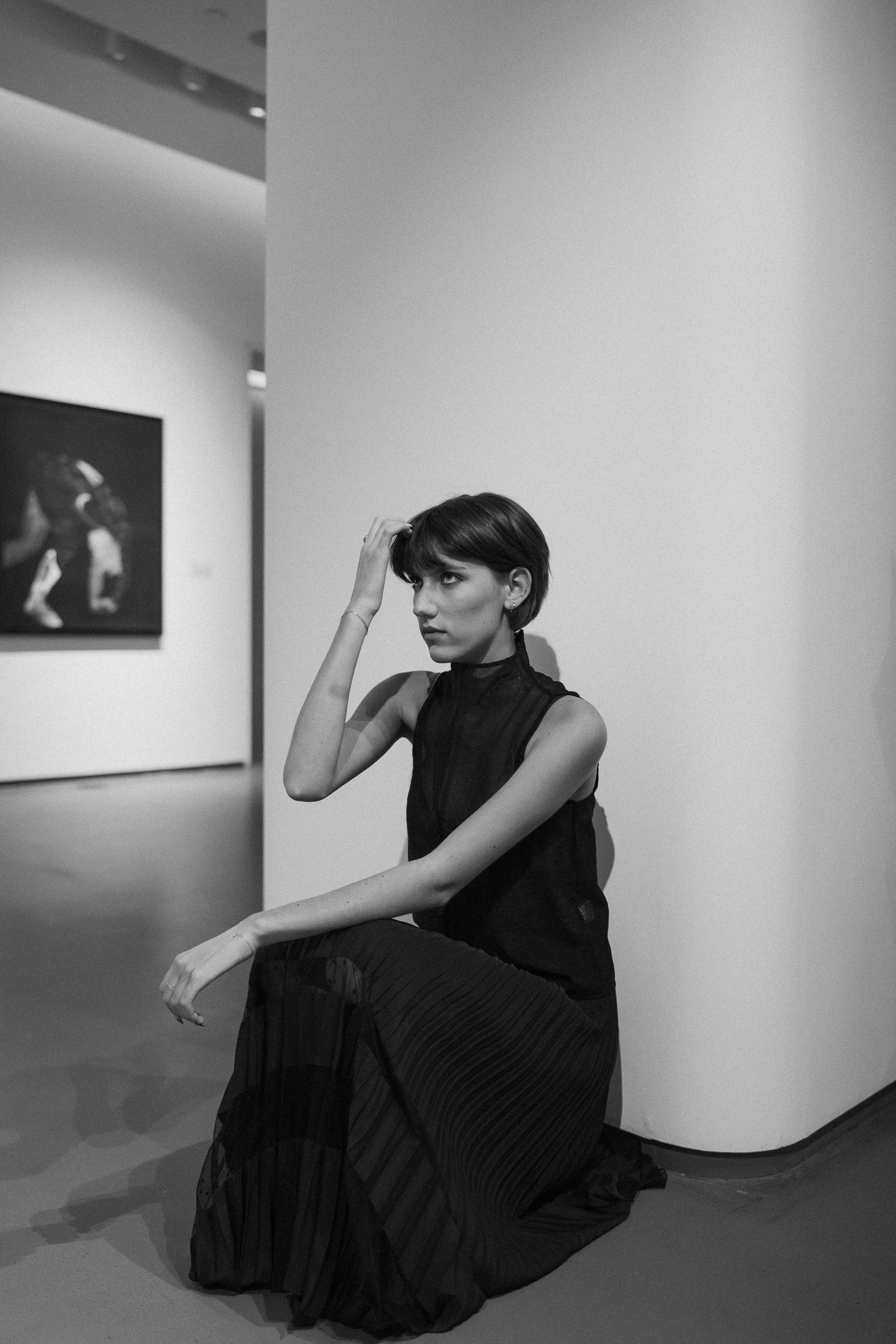 Cana, seated in a gallery, in a long black sleeveless dress